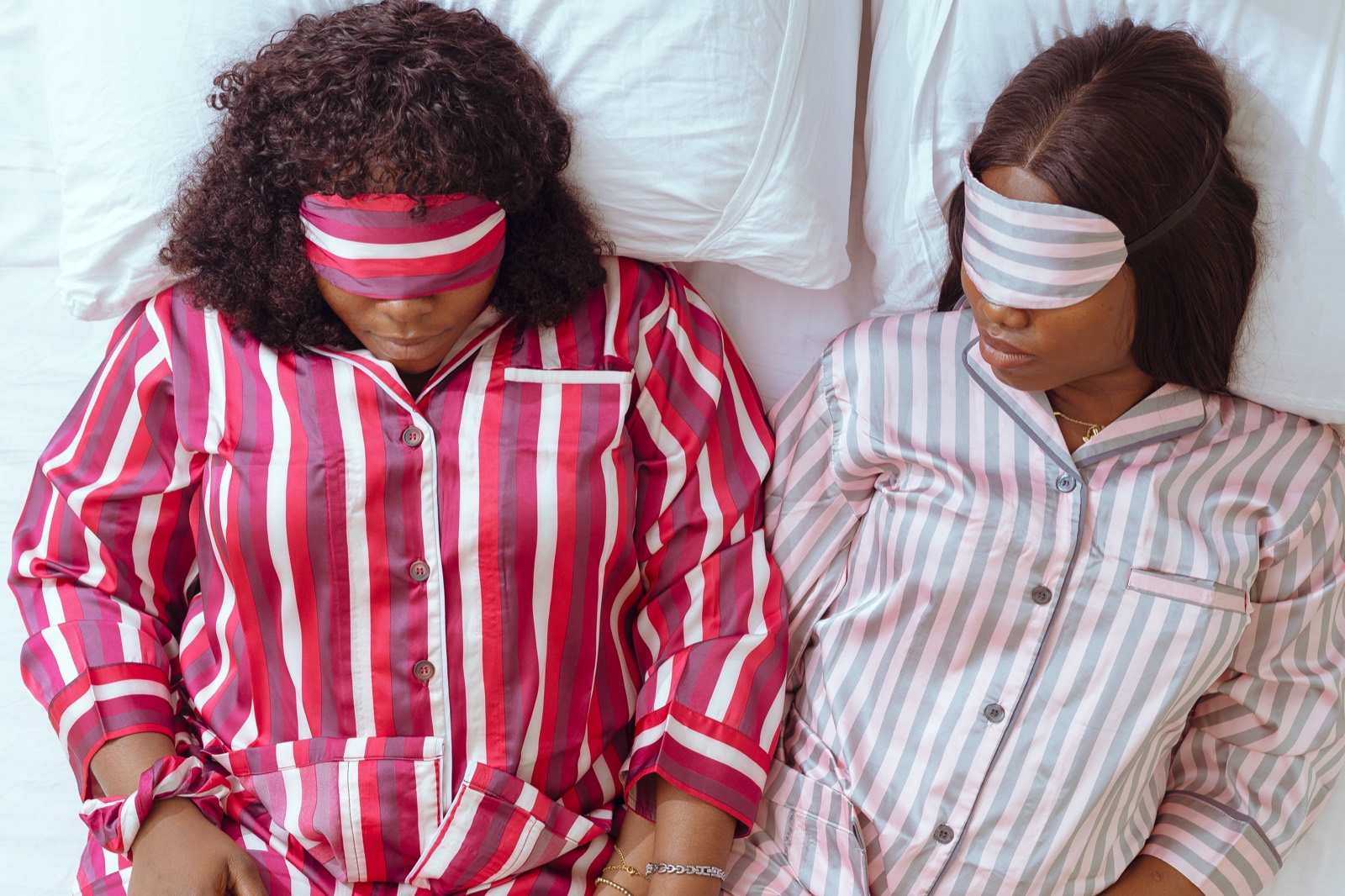 Two women resting in crimson and dove striped satin pajamas